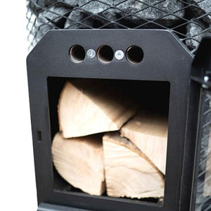 A close-up view shows the open firebox of a Cozy Heat wood-burning sauna stove. The black cast-iron door is swung open to the right side, revealing several large, split pieces of dry firewood neatly stacked inside the dark chamber. Directly above the main opening, the matte black frame features 3 small, circular air vents arranged horizontally, secured w/ two screws. In the background, just above the firebox structure, the wire mesh cage & stacked grey sauna stones are partially visible.