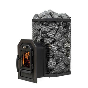 A Cozy Heat Thru-Wall wood-burning sauna stove is shown from an angled perspective against a plain white background. The unit features a tall, octagonal black wire mesh cage packed to the top with grey sauna stones. Extending forward to the left is the structural firebox tunnel designed for through-wall installation, ending with a closed black cast-iron door. Bright orange flames are visible actively burning inside the glass viewing window beneath the embossed "COZY" brand name.