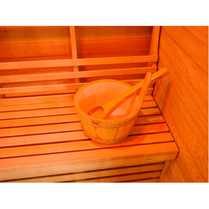 The image shows a close-up view of a traditional wooden bucket and ladle resting on the slatted wooden bench inside the sauna, with the wall paneling and backrest in the background.