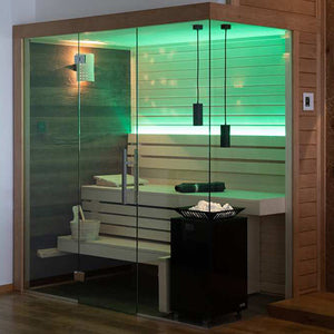 Glass-enclosed sauna with wood slat benches, green LED backlit wall panel, hanging pendant lights, control panel, wall-mounted shower fixture, and black heater with stone tray.