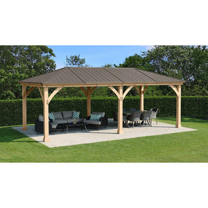 12 x 24 Meridian Gazebo - exterior grade cedar coated in natural cedar-color stain with coffee brown colored aluminum roof, 6” x 6” Posts with classic plinths, Heavy, curved corner gussets placed in a garden isometric view