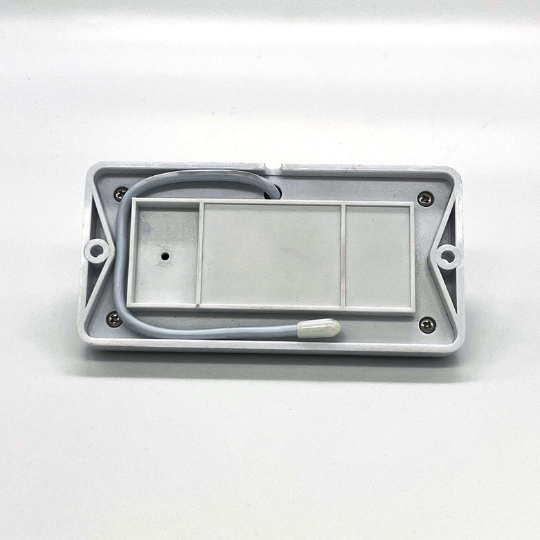The grey rectangular underside of a sensor module rests horizontally against a white background, showing its recessed compartments, four corner screws, mounting holes on each end, and a grey wire tucked inside.