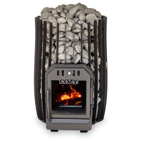 A barrel-shaped, black metal wood-burning sauna stove filled to the top with rounded grey stones. The stove body consists of vertical metal bars acting as a cage, exposing the textured rocks packed tightly inside. At the bottom center is a dark grey metal door with the word 'COZY' embossed above a square glass viewing window. Bright orange and yellow flames glow vividly inside the firebox, visible through the window against a plain white background.