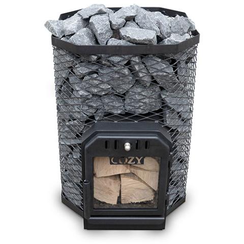 A Cozy Heat 18kW wood-burning sauna stove is shown from a front perspective against a plain white background. The stove features a multi-sided, octagonal outer cage made of black wire mesh that is filled to the top with grey sauna stones. A black cast-iron firebox door is integrated at the base, featuring a large glass viewing window that reveals stacked pieces of firewood inside the chamber and the "COZY" brand name visible just above the wood.