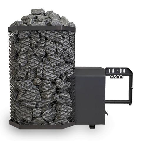 A Cozy Heat 18kW Thru-Wall wood-burning sauna stove is shown from a side perspective against a plain white background. The left portion of the unit features the tall, octagonal black wire mesh cage packed to the top with grey sauna stones. Extending horizontally to the right is the structural firebox tunnel designed for through-wall installation, ending with the open frame of the black cast-iron door that features the embossed "COZY" brand name.