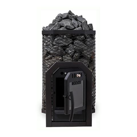 A Cozy Heat Thru-Wall wood-burning sauna stove is shown from a front perspective against a plain white background. The stove features a tall, octagonal black wire mesh cage packed to the top with textured grey sauna stones. At the front base, the structural firebox tunnel designed for through-wall installation is visible, featuring a black cast-iron frame with its glass-windowed door swung wide open to the right to reveal the dark interior chamber.