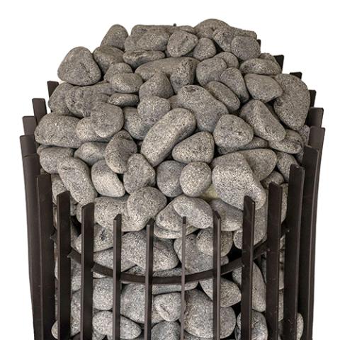 A high-angle, close-up shot focusing on the top section of a black metal sauna stove against a white background. The frame consists of thick, vertical rectangular metal slats arranged in a circular cage formation. Inside, the stove is packed tightly with a dense mound of rounded, textured grey stones that pile significantly over the top rim of the metal cage structure.