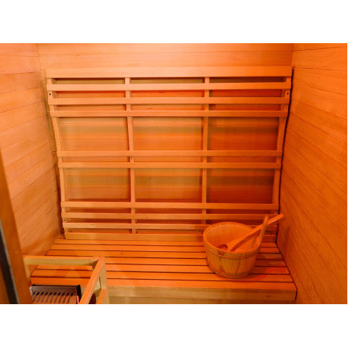 The interior of the sauna features warm wooden wall paneling, a slatted wooden bench, a wide wooden backrest mounted against the wall, a traditional wooden bucket with a ladle sitting on the bench, and a protective wooden guard frame enclosing the heater in the lower left corner.