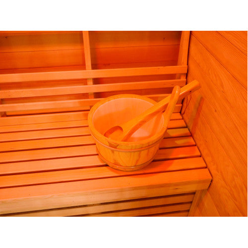 The image shows a close-up view of a traditional wooden bucket and ladle resting on the slatted wooden bench inside the sauna, with the wall paneling and backrest in the background.