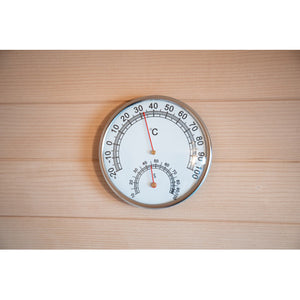 The image shows a round dual-gauge thermometer and hygrometer mounted on the wooden wall paneling, with the temperature needle pointing near 34°C and the humidity needle pointing to 50%.