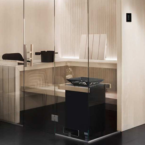 Glass-enclosed sauna with light wood slat benches, backrest, backlit paneling, wall-mounted control panel, and black heater with stone tray.