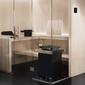 Glass-enclosed sauna with light wood slat benches, backrest, backlit paneling, wall-mounted control panel, and black heater with stone tray.