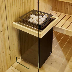 Black EOS sauna heater with wood-trimmed top and stone tray filled with white sauna rocks, installed in wood-paneled sauna with slatted bench and glass door.