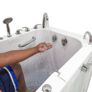 Close-up of a man testing running water from the chrome faucet in a white walk-in bathtub, with handheld shower, control panel, and grab bar visible.