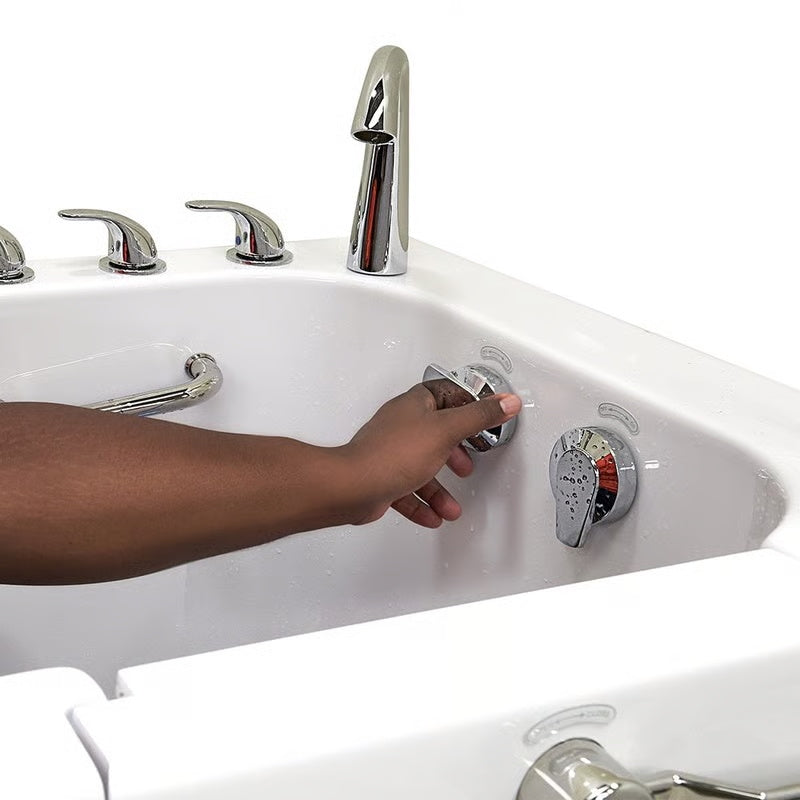 Close-up of a hand adjusting a chrome hydrotherapy jet control inside a white walk-in bathtub, with faucet handles and grab bar visible.