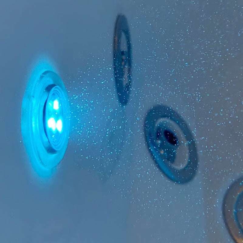 Close-up underwater view of an illuminated blue chromotherapy light and hydrotherapy jets inside a walk-in bathtub filled with water.
