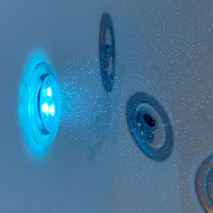 Close-up underwater view of an illuminated blue chromotherapy light and hydrotherapy jets inside a walk-in bathtub filled with water.