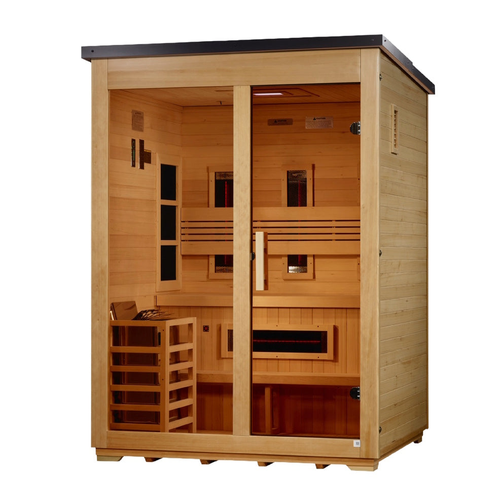 A freestanding light-tan wooden sauna cabin with a dark gray sloped roof, viewed from a slight right angle. The glass facade includes a door on the right with a vertical wooden handle. Inside, dark infrared panels with glowing red centers are visible: two vertical panels on the back wall behind a horizontal slatted backrest, one horizontal panel underneath the two-tier bench, and three square panels on the left side wall. A wooden-slat heater cage rests on the bottom left under an overhead ceiling LED light