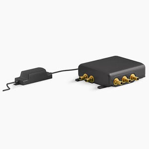 A rectangular Kohler digital thermostatic shower valve system in matte black, shown on a white background. The main control module box features protruding brass inlet and outlet ports on two sides. A black cable connects the valve to a smaller, matching matte black rectangular power supply adapter block with a power cord extending from its left end.