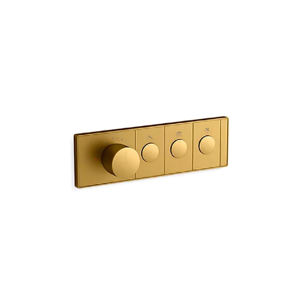 A horizontal, rectangular Kohler K-26347-9 Anthem mechanical thermostatic valve control in brushed brass, angled slightly right against a white background. The sleek faceplate features four cylindrical knobs in a row. The first knob on the left is much larger and thicker, surrounded by small indicator dots for temperature. To its right are three smaller, identical control knobs, each centered within a rectangular segment containing a small icon above it.