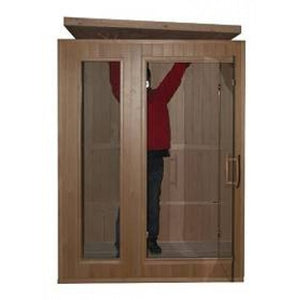 The image shows a person in a red jacket and dark pants standing inside the front frame of the sauna while positioning or adjusting the roof panel during the assembly process.