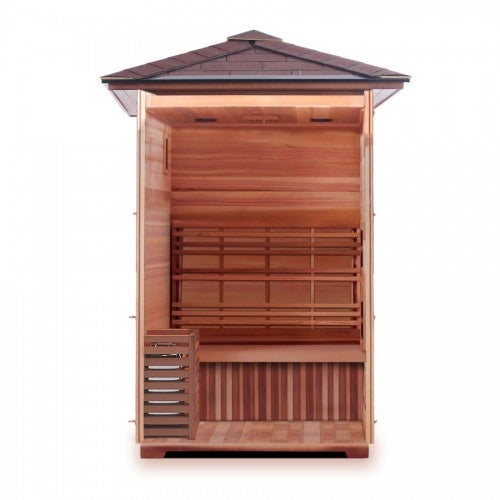 The open front view of the SunRay Eagle 2-Person Outdoor Traditional Wet/Dry Sauna (HL200D1) displays its spacious interior layout, highlighting the wooden flooring, the bench seating with a slatted backrest, the heater enclosed in a protective wooden guard on the left, and the paneled ceiling with lighting fixtures beneath the pitched shingle roof.