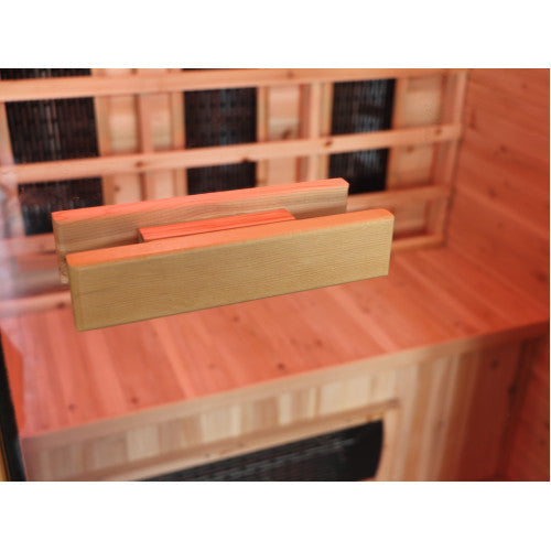 The image shows a close-up view of the wooden door handle mounted on the glass entry door of the sauna, with the warm wooden interior, slatted backrest, bench, and lower heating panel visible in the background.