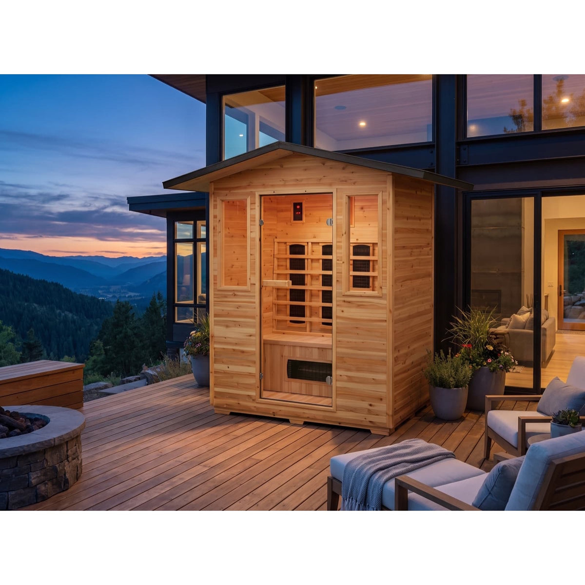 The SunRay Sauna Grandby 3-Person Outdoor Infrared Sauna (model HL300D3) set up on a wooden deck overlooking mountain views at sunset, featuring horizontal cedar wood paneling, an overhanging shingled roof, a glass door with side windows, and outdoor lounge furniture.