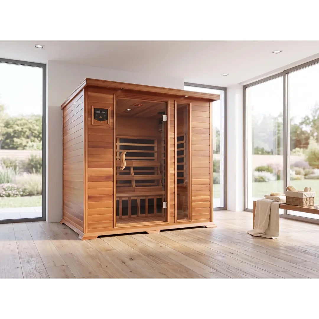 The SunRay Savannah 3-Person Infrared Cedar Sauna (model HL300K_2) installed in a room with a soft pink wall and gray floor, featuring rich dark-stained cedar wood construction, a front glass door with a side window panel, a digital control panel, and an exercise bike nearby.