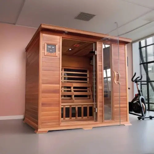 The SunRay Savannah 3-Person Infrared Cedar Sauna (model HL300K_2) installed in a room with a soft pink wall and gray floor, featuring rich dark-stained cedar wood construction, a front glass door with a side window panel, a digital control panel, and an exercise bike nearby.
