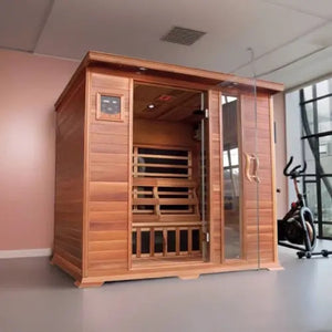 The SunRay Savannah 3-Person Infrared Cedar Sauna (model HL300K_2) installed in a room with a soft pink wall and gray floor, featuring rich dark-stained cedar wood construction, a front glass door with a side window panel, a digital control panel, and an exercise bike nearby.