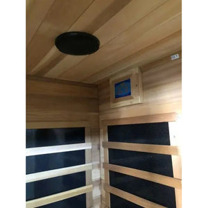 An interior perspective of the SunRay Savannah 3-Person Infrared Cedar Sauna (model HL300K_3), showing a dark round speaker mounted on the cedar wood ceiling and adjacent interior walls featuring infrared heating panels behind slatted guards and a control panel.