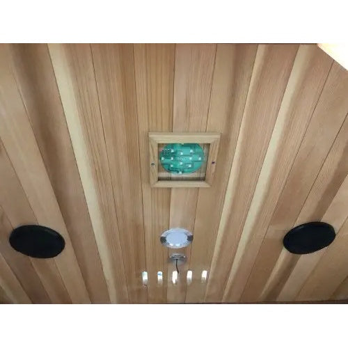 An interior perspective of the SunRay Savannah 3-Person Infrared Cedar Sauna (model HL300K_4), showing the cedar wood ceiling outfitted with two black round speakers, a central recessed light, ventilation slots, and a square chromatherapy lighting panel.