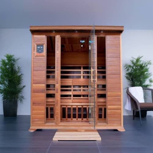 The SunRay Sequoia 4-Person FAR Infrared Indoor Sauna (model HL400K_2) installed in a room with dark tiled flooring, a pale ceiling, and a dark wall, featuring a rich dark-stained wood finish, a glass door with side window panels, a digital control panel, and decorative potted plants and a chair nearby.