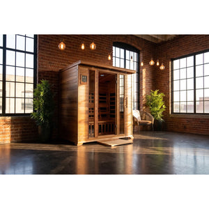 The SunRay Sequoia 4-Person FAR Infrared Indoor Sauna (model HL400K_3) set up in an industrial loft with exposed red brick walls, large grid windows, pendant Edison bulb lighting, and polished concrete flooring.