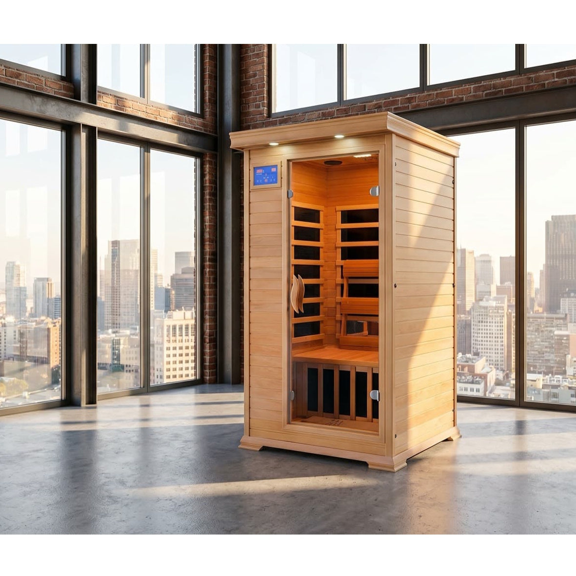 An indoor, light-brown cedar infrared sauna stands in a brightly lit room with a wooden floor. The sauna features a glass door, a digital control panel near the top left, and a wooden bench inside. Next to it are a tall shelving unit with plants, a woven basket holding rolled yoga mats and towels, a small wooden side table with a potted plant, and an armchair.