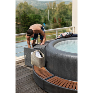 MSpa Curved Wicker Step for Round Spa color grey beside the round spa with one male located outdoor